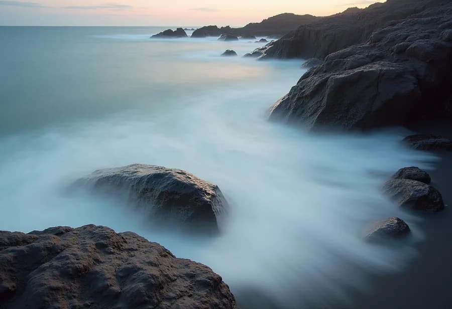 A long exposure of pale sea washing over dark volcanic rock